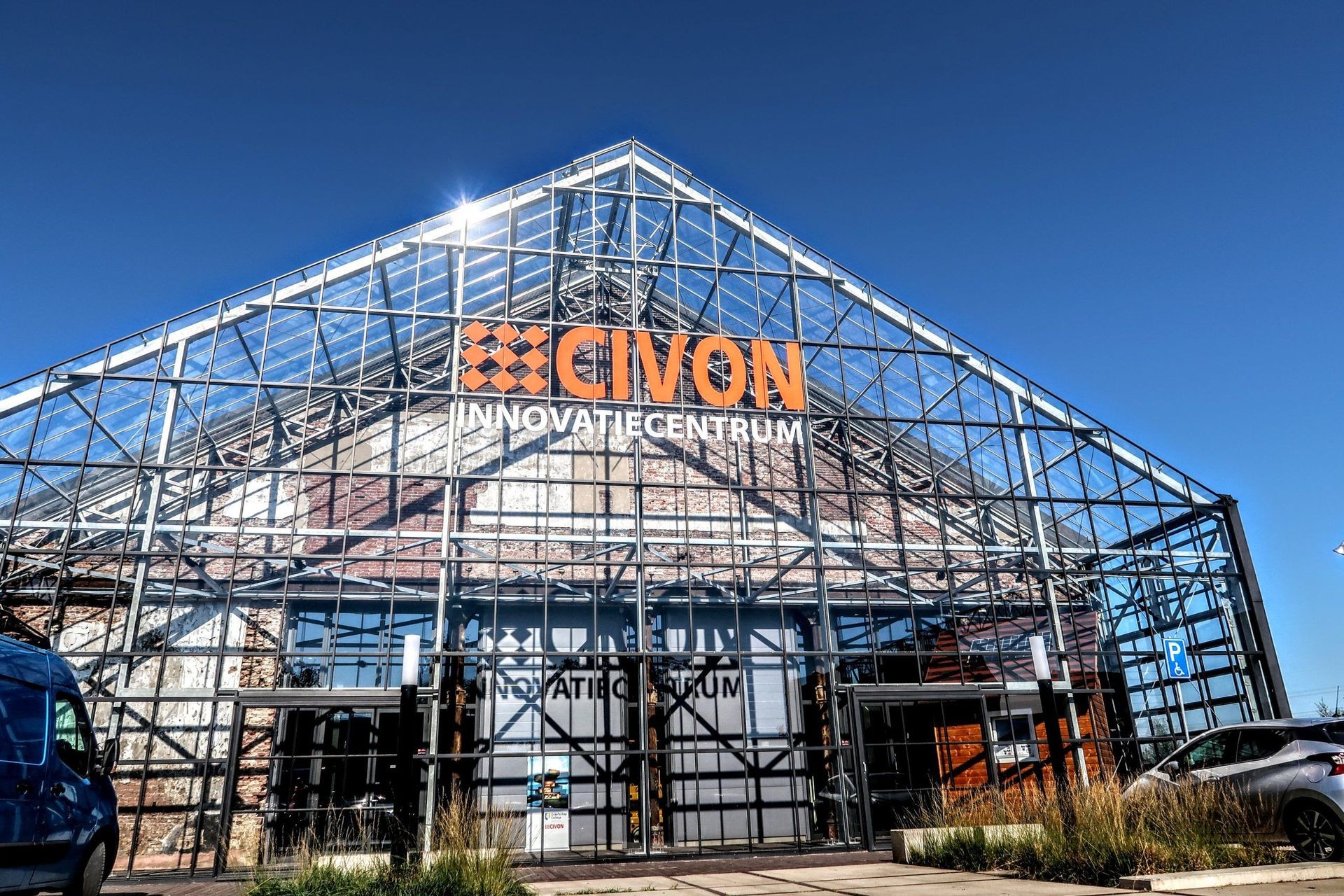 Glass building facade with 'CIVON Innovatiecentrum' sign under clear blue sky.